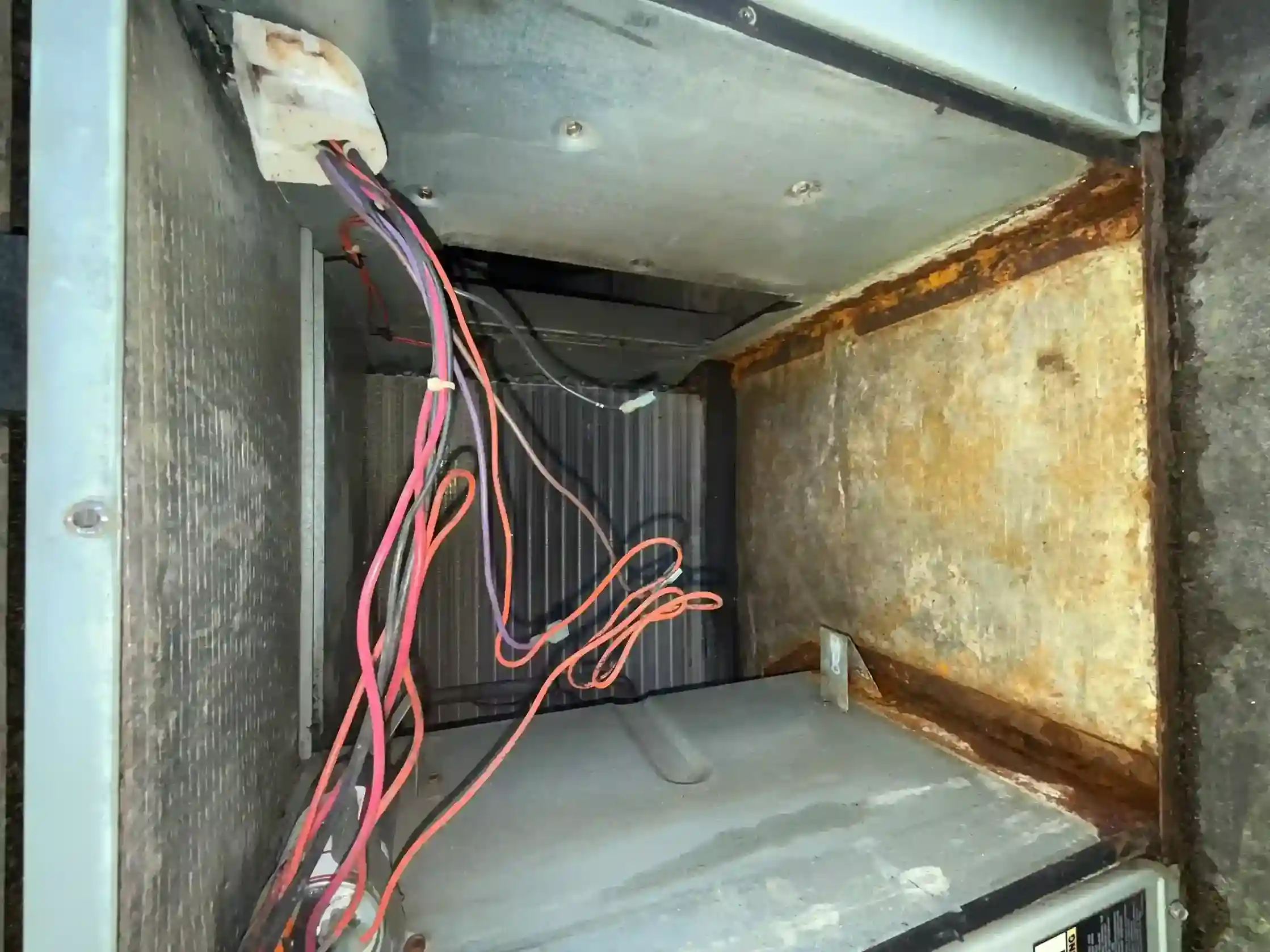 Air handler interior showing evaporator A-coil, loose wiring, and extreme rust on housing wall