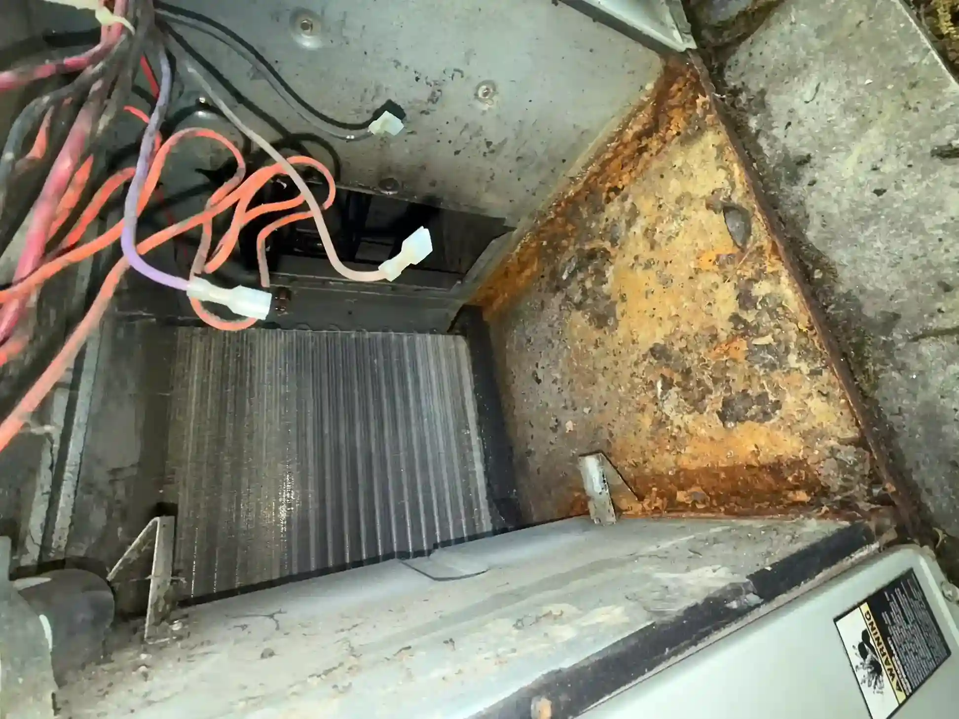 Open air handler cabinet showing dirty evaporator coil, rusted housing, and loose control wiring